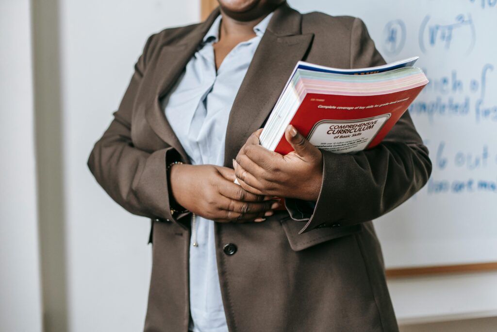 pexels-photo-5905489-5905489 A professional educator in a formal setting holding a curriculum book in front of a whiteboard.